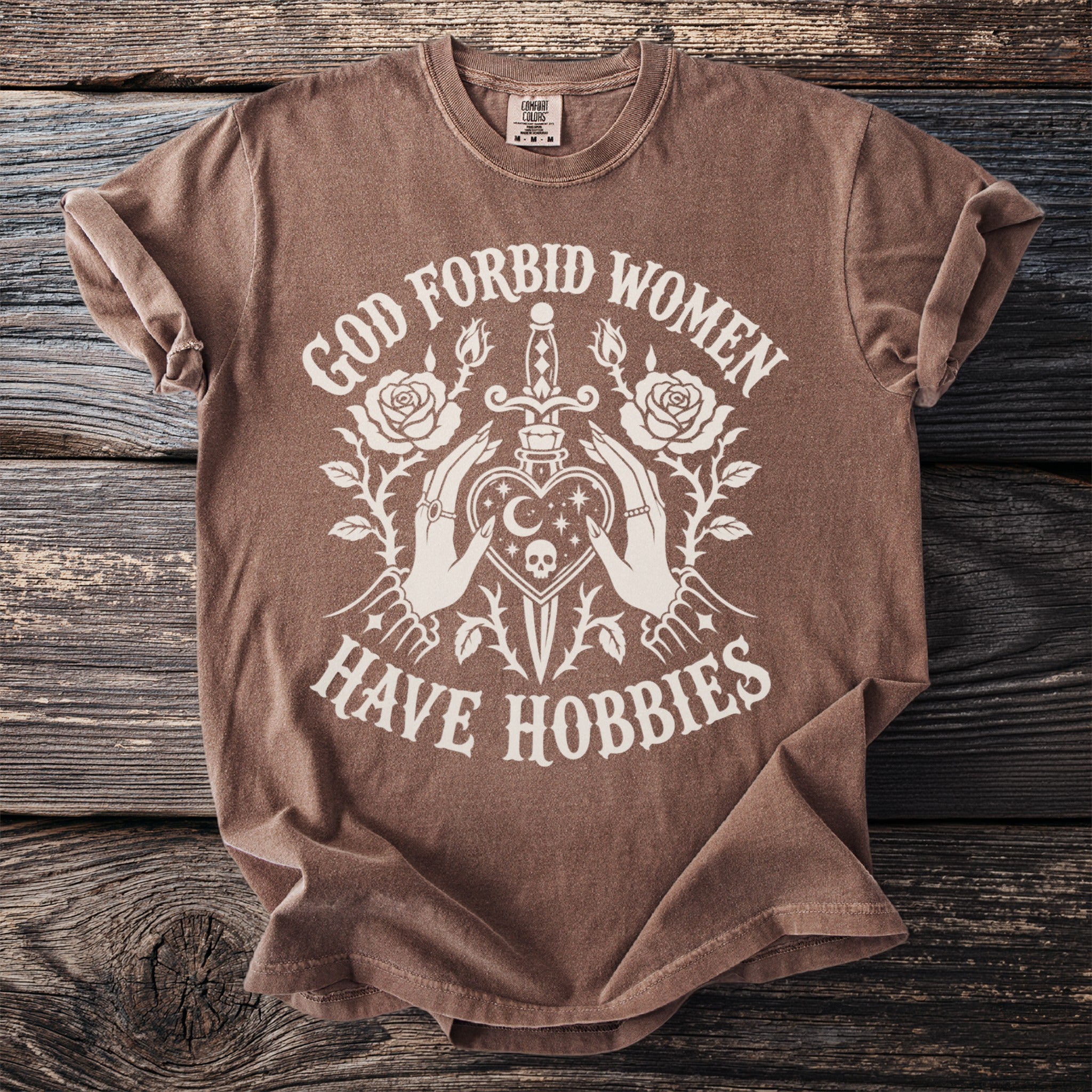 Brown t-shirt with white graphic design and text that reads "God forbid women have hobbies".