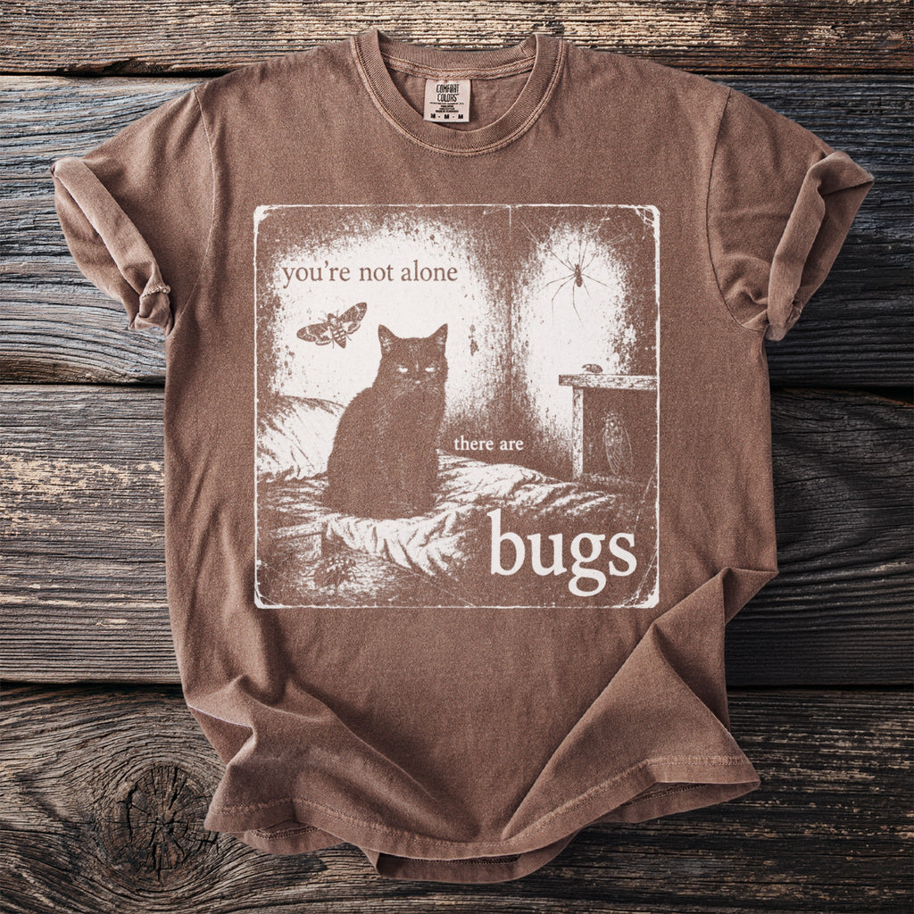 Brown t-shirt with print of a black cat, moth, spider, and text "you're not alone there are bugs".