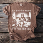 Brown t-shirt with a graphic of a werewolf sitting on a couch with drinks and pizza.