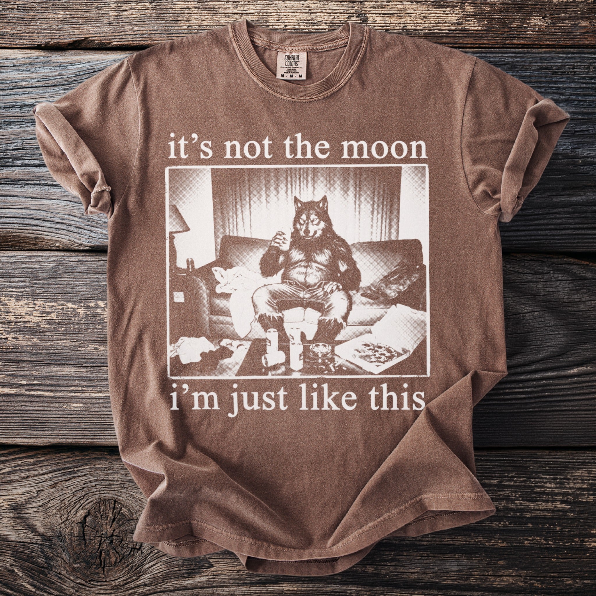 Brown t-shirt with a graphic of a werewolf sitting on a couch with drinks and pizza.