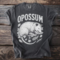 Dark gray t-shirt with "OPOSSUM" text and opossum illustration with leaves and insects.