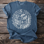Blue t-shirt with white illustration of stacked books, key, moth, crescent moon, and candle.