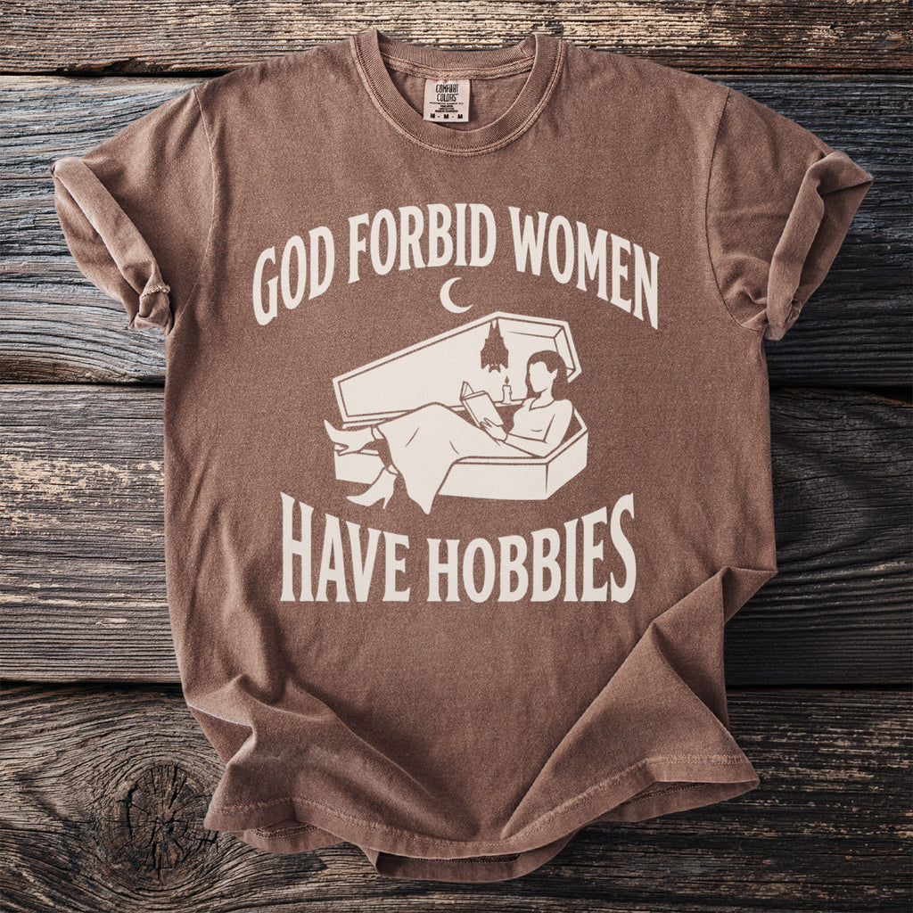 Brown t-shirt with "God forbid women have hobbies" text and coffin graphic.