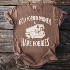 Brown t-shirt with "God forbid women have hobbies" text and coffin graphic.