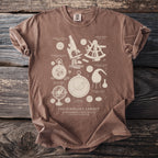 Brown t-shirt printed with "The Scholar's Cabinet" design featuring scientific instruments.