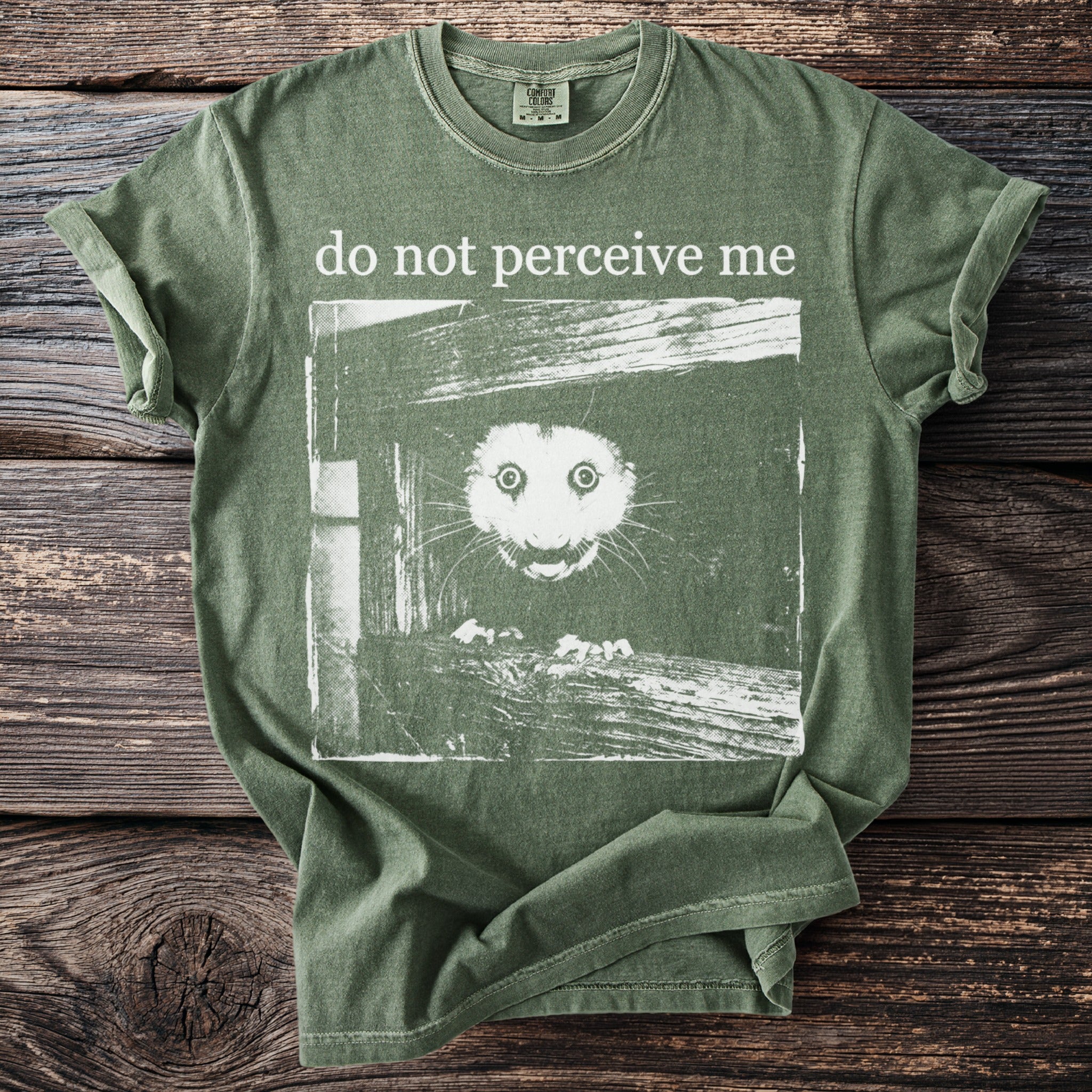 Olive green T shirt with a wide eyed bushbaby and “do not perceive me” text.