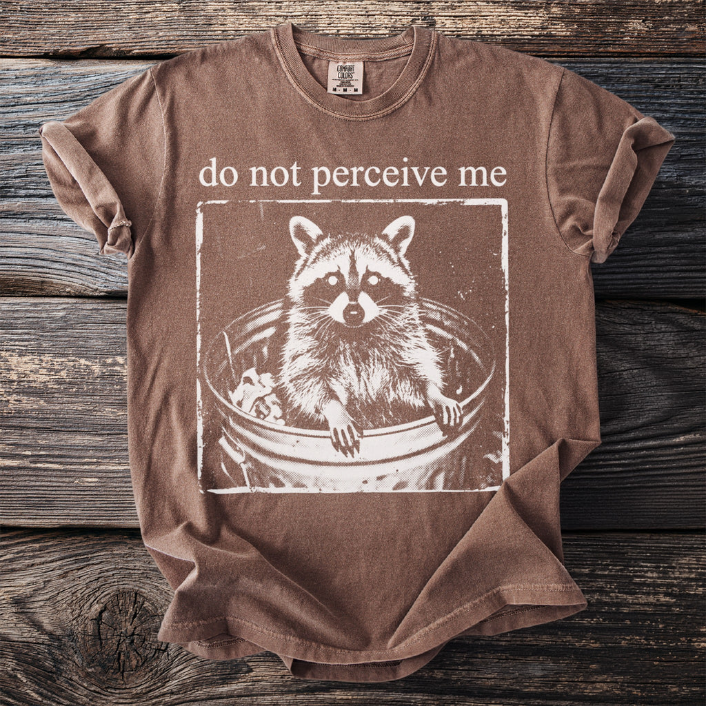 Brown t-shirt with white raccoon in a trash can and text "do not perceive me."