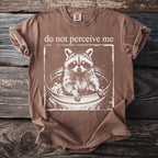Brown t-shirt with white raccoon in a trash can and text "do not perceive me."