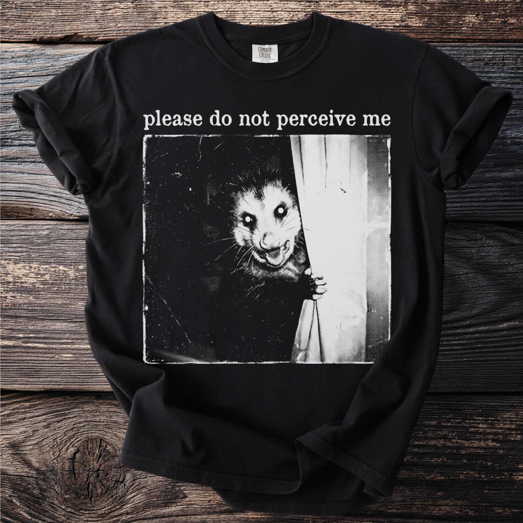 Black t-shirt with a vintage-style graphic of a possum peeking from behind a curtain that reads "please do not perceive me".