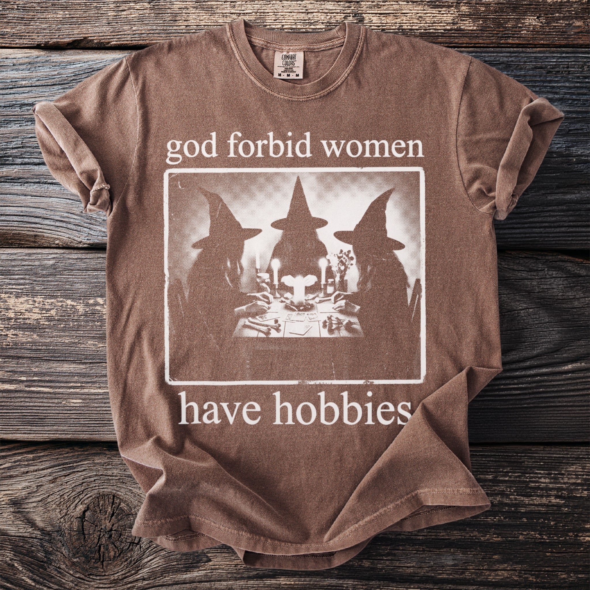 Brown t-shirt with "god forbid women have hobbies" and a vintage witch graphic.