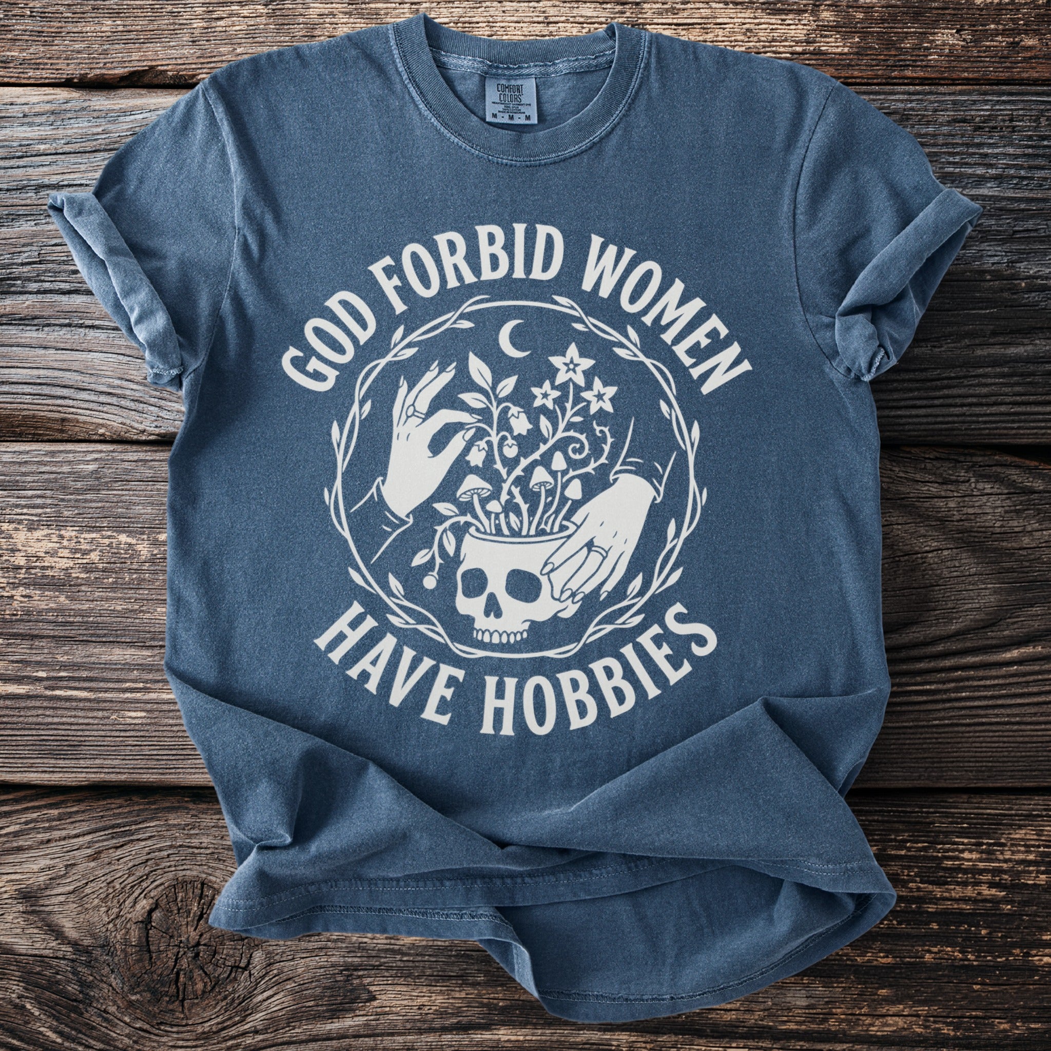Blue t-shirt with white text "GOD FORBID WOMEN HAVE HOBBIES" and skull graphic.