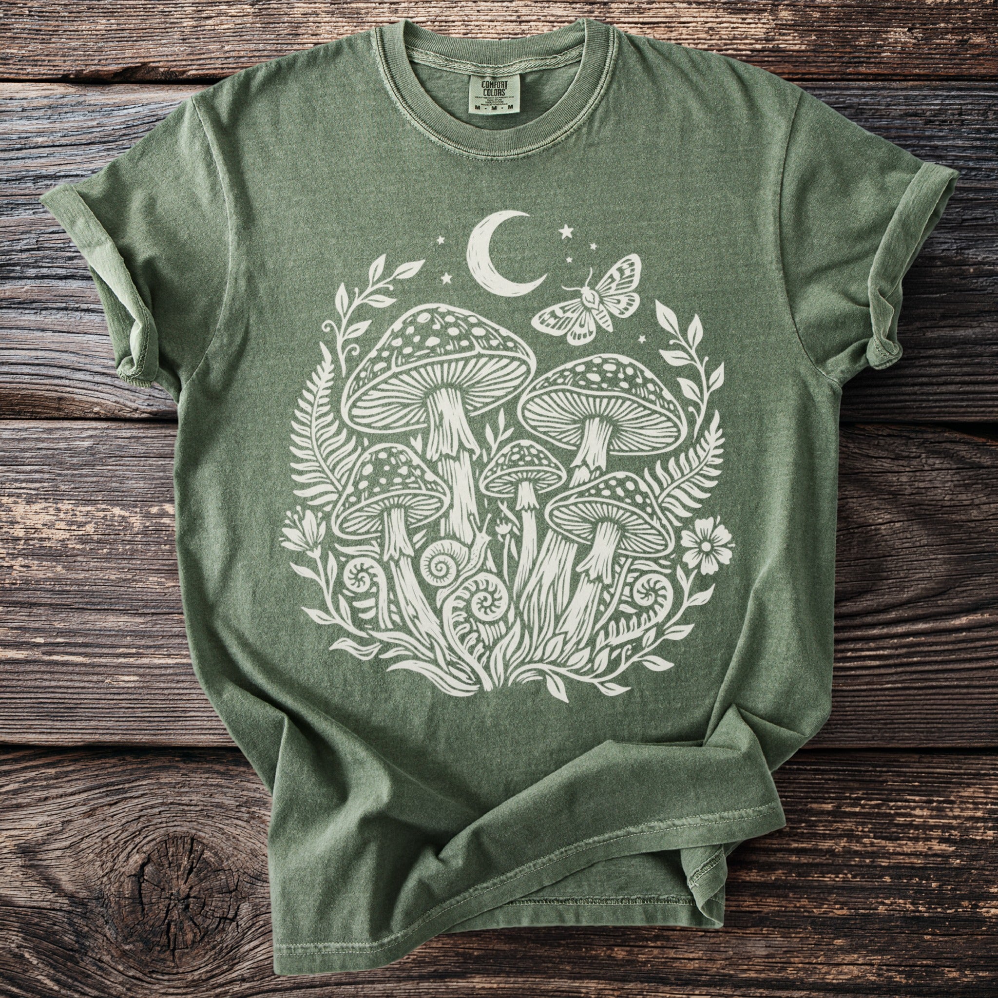 Olive green t-shirt with white mushroom forest, moon, stars, and moth graphic.