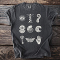 Dark grey t-shirt with white graphics of an eye, lighthouse, octopus tentacle, diver helmet, shell, wave, key, moth, and hand.