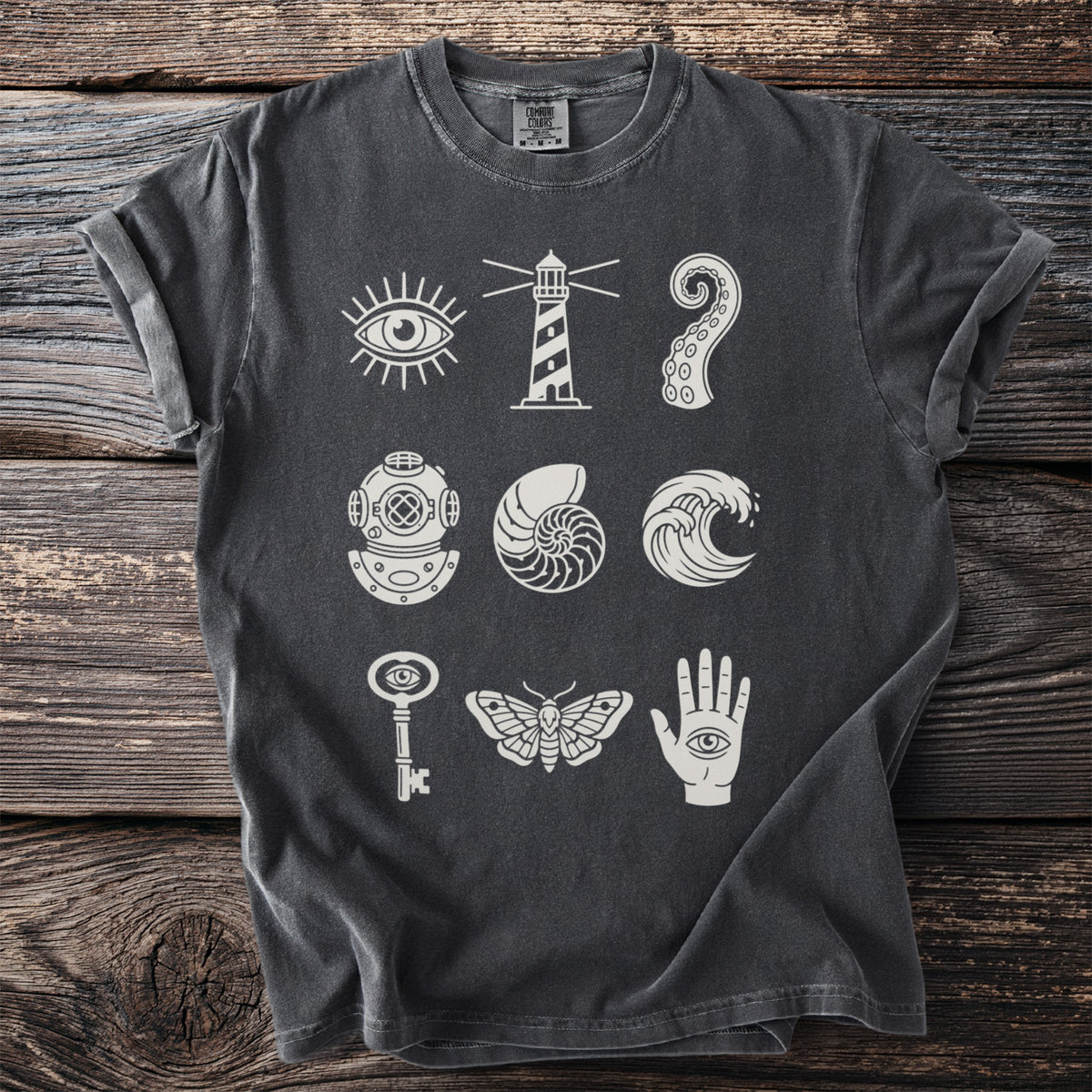 Dark grey t-shirt with white graphics of an eye, lighthouse, octopus tentacle, diver helmet, shell, wave, key, moth, and hand.