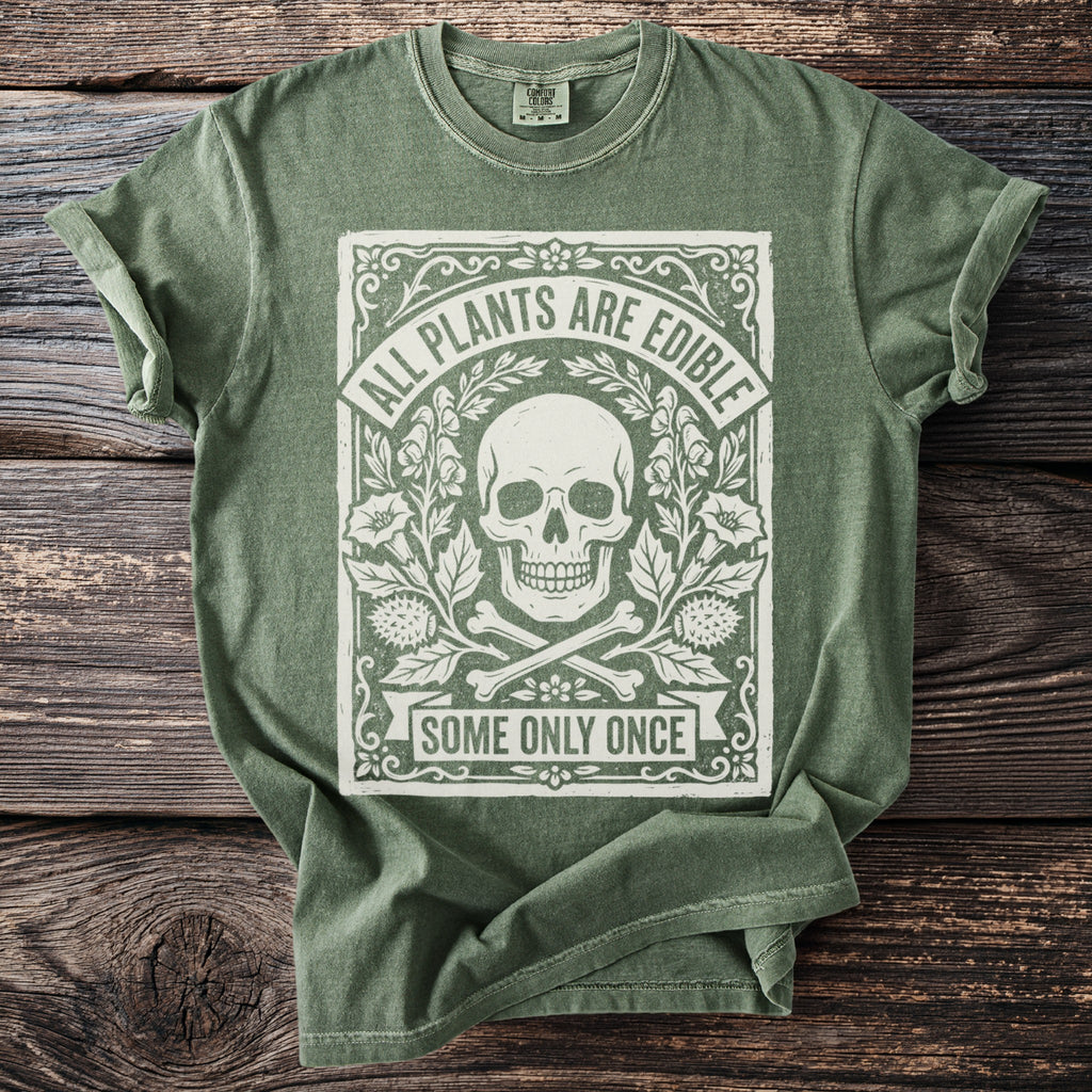 Green t-shirt with white graphic of a skull, bones, flowers, and text saying "ALL PLANTS ARE EDIBLE SOME ONLY ONCE".