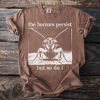 Brown t-shirt with a graphic of a cockroach and text "the horrors persist but so do i".