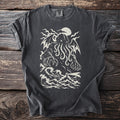 Pepper grey t-shirt with a cream print of a winged tentacled sea giant over crashing waves and a lighthouse.