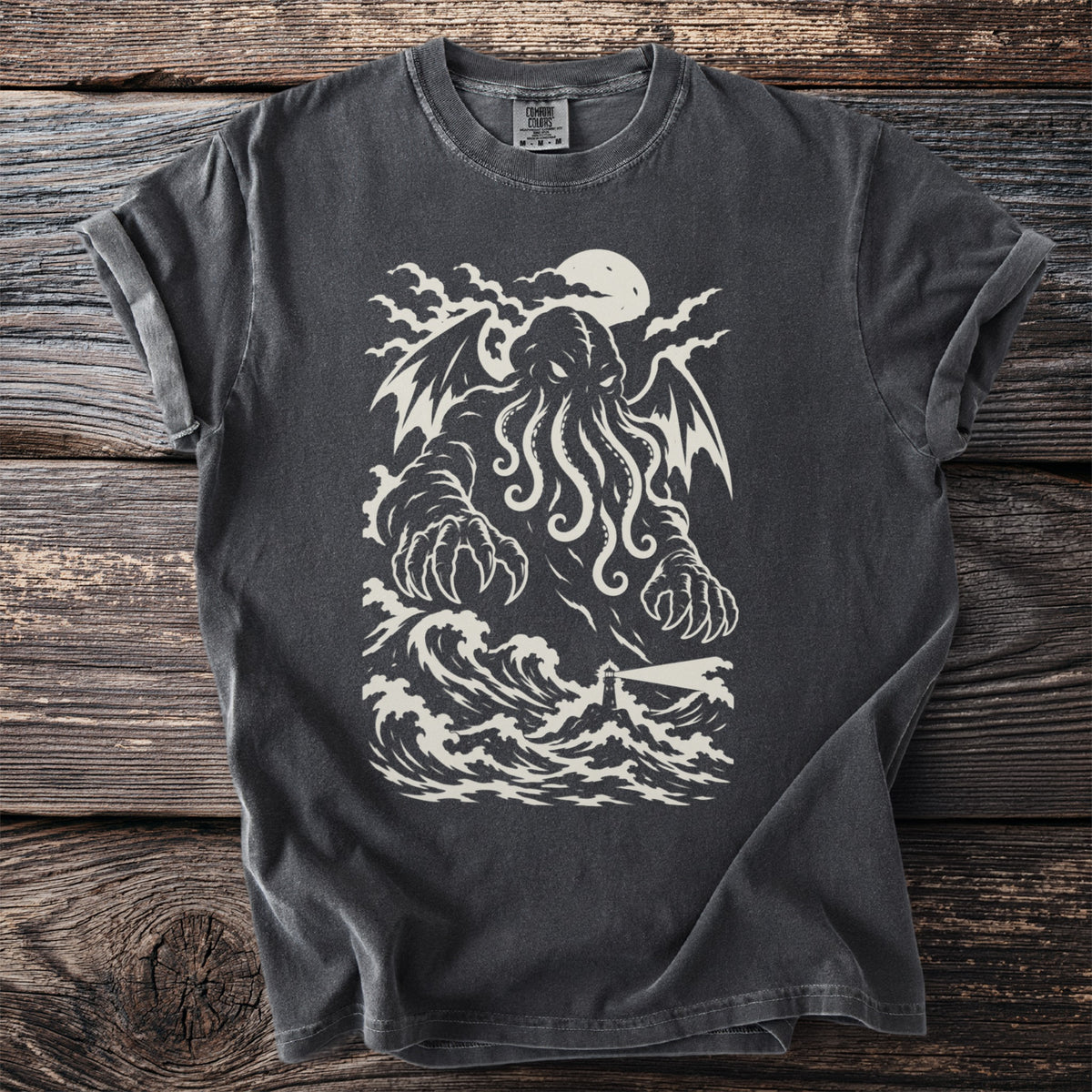 Pepper grey t-shirt with a cream print of a winged tentacled sea giant over crashing waves and a lighthouse.