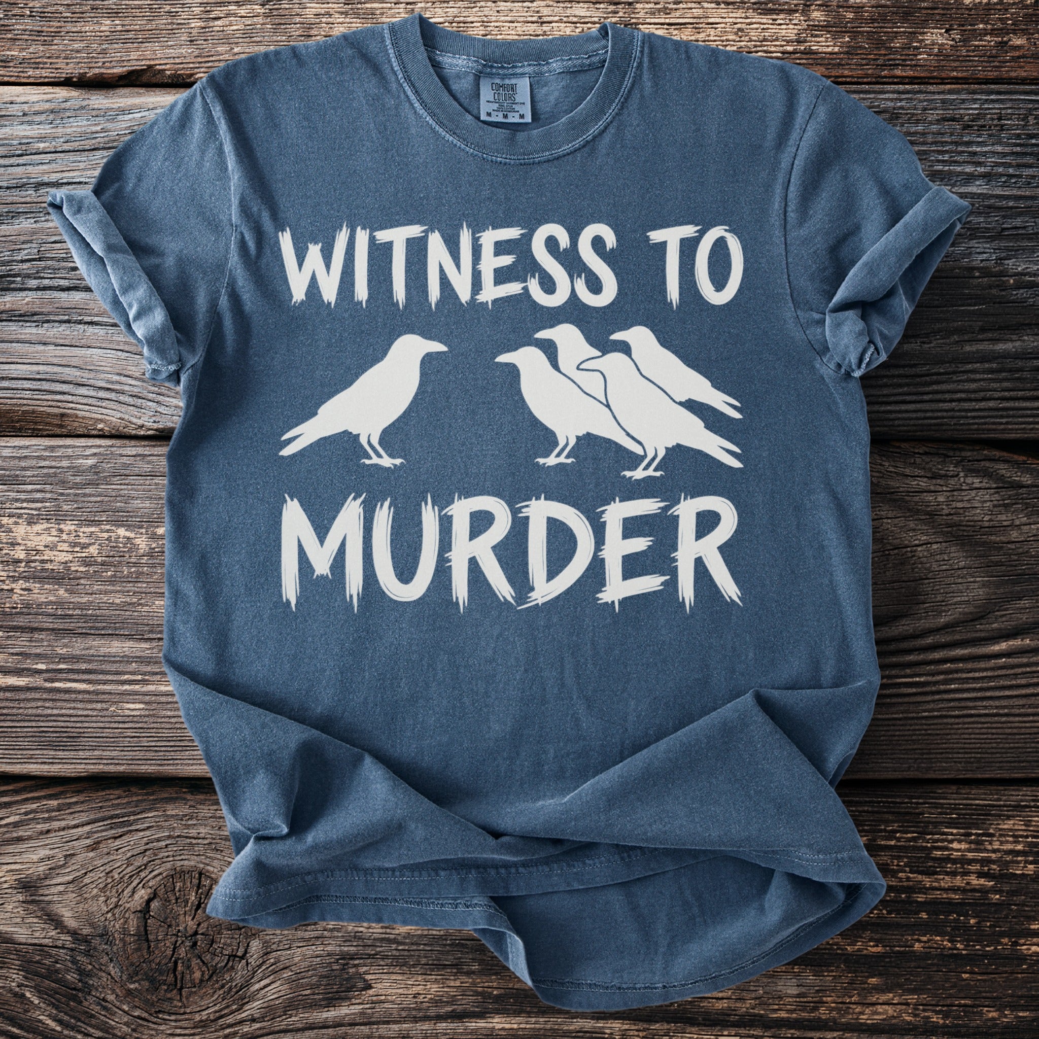 Blue t-shirt with white text "WITNESS TO MURDER" and silhouette of birds.