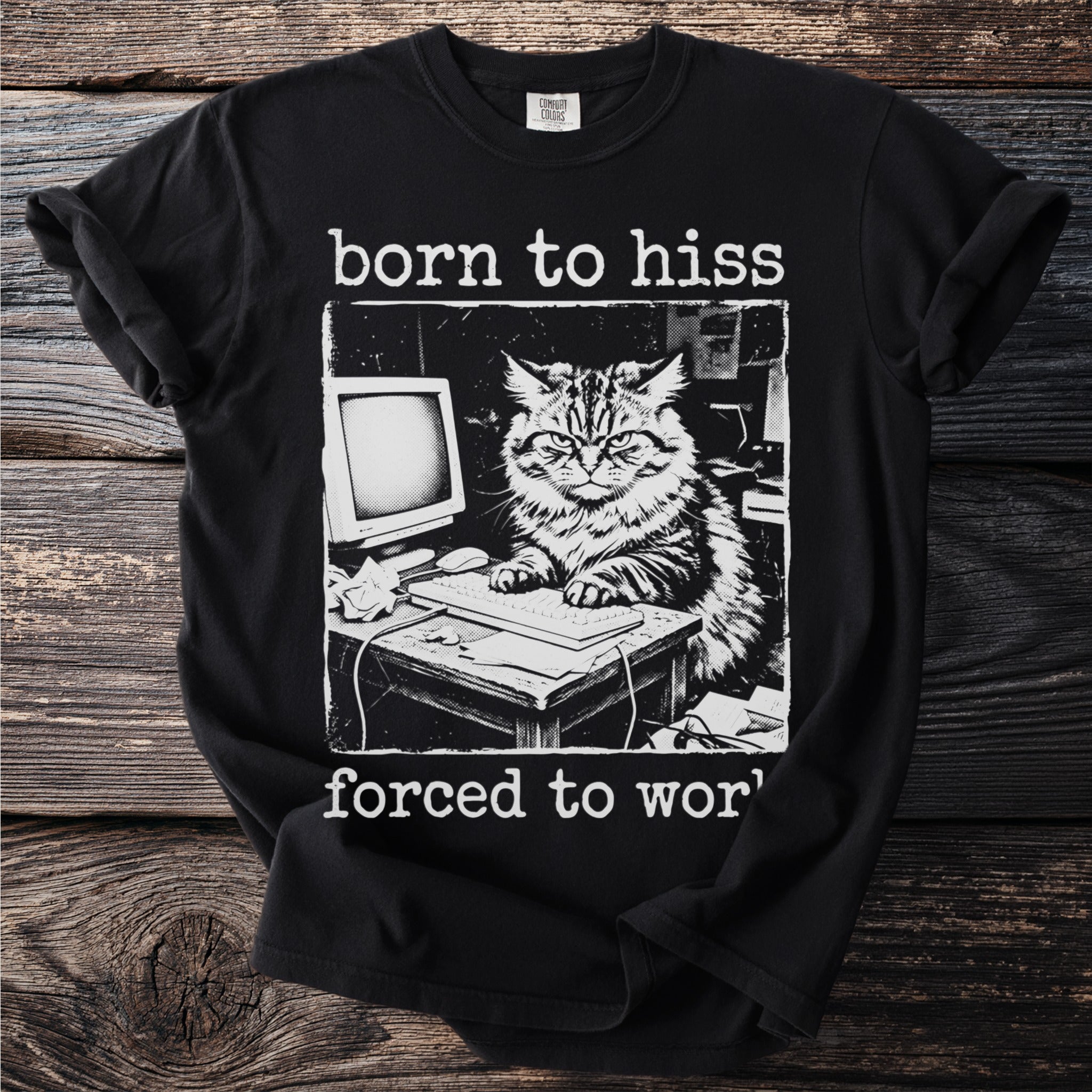 Black t-shirt with a vintage illustration of an angry cat at a desk with a computer and keyboard. Text reads "born to hiss forced to wor'".