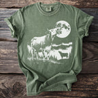 Green t-shirt with white graphic of cows and a full moon at night.