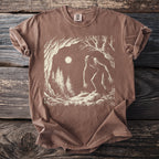 Brown Comfort Colors t-shirt featuring a Bigfoot in a forest scene under a full moon.