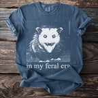 Blue t-shirt with opossum graphic and "in my feral era" text.