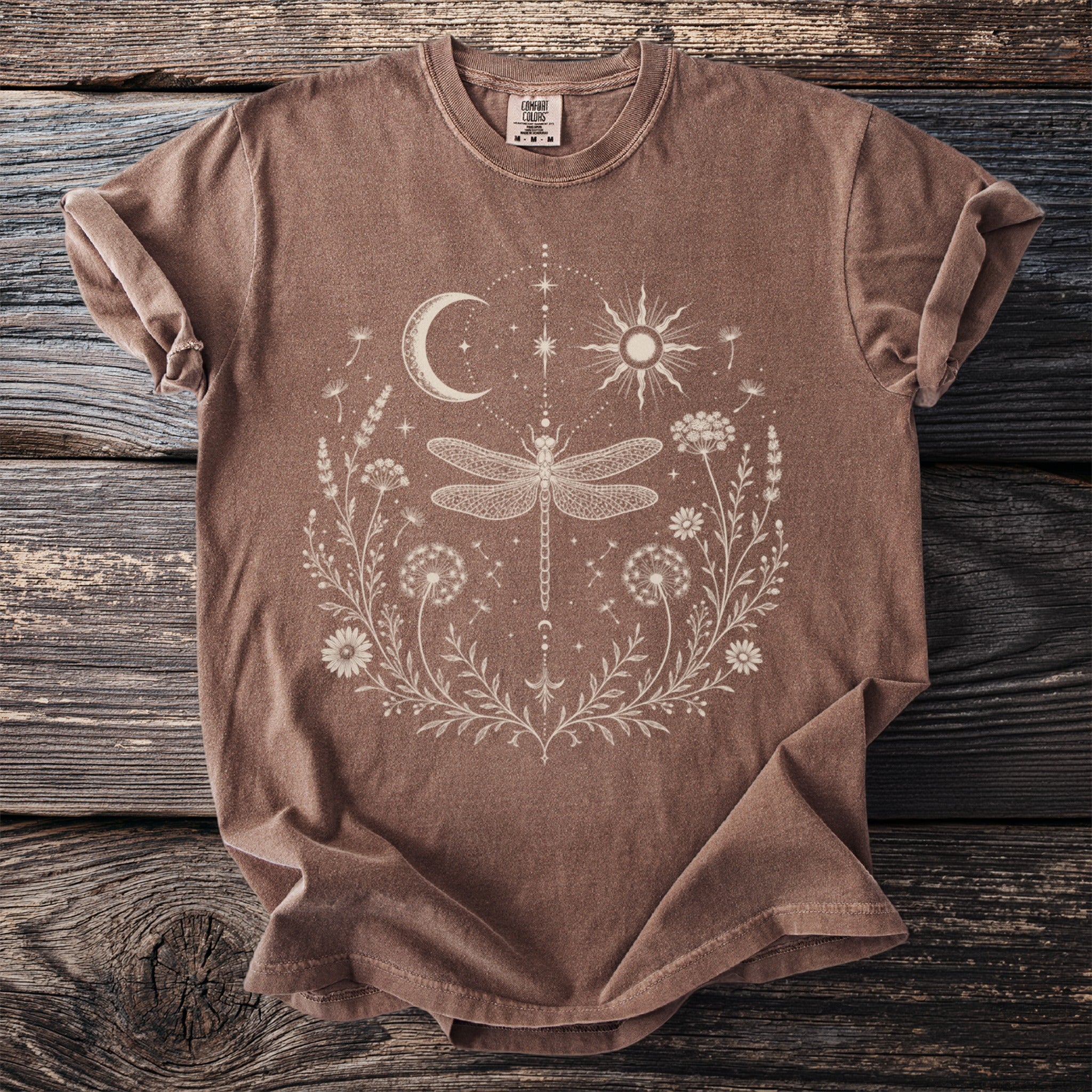 Brown t-shirt with a white line art design of a dragonfly and celestial elements.
