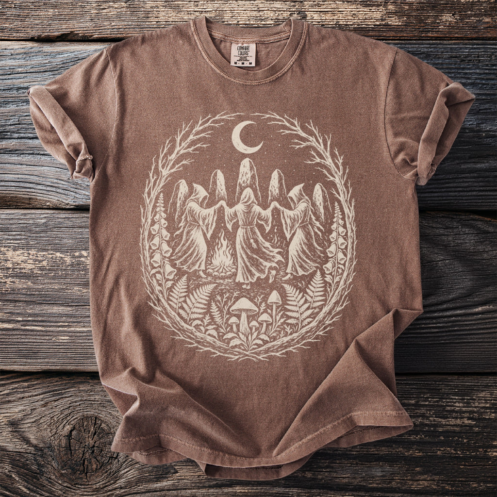 T-shirt with circle design of robed figures, moon, mushrooms, and foliage.