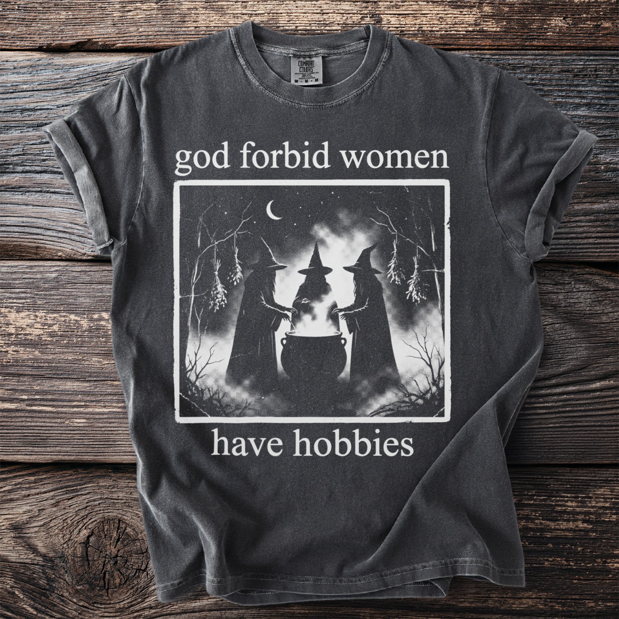 Graphic t-shirt with slogan "god forbid women have hobbies" and image of three witches.