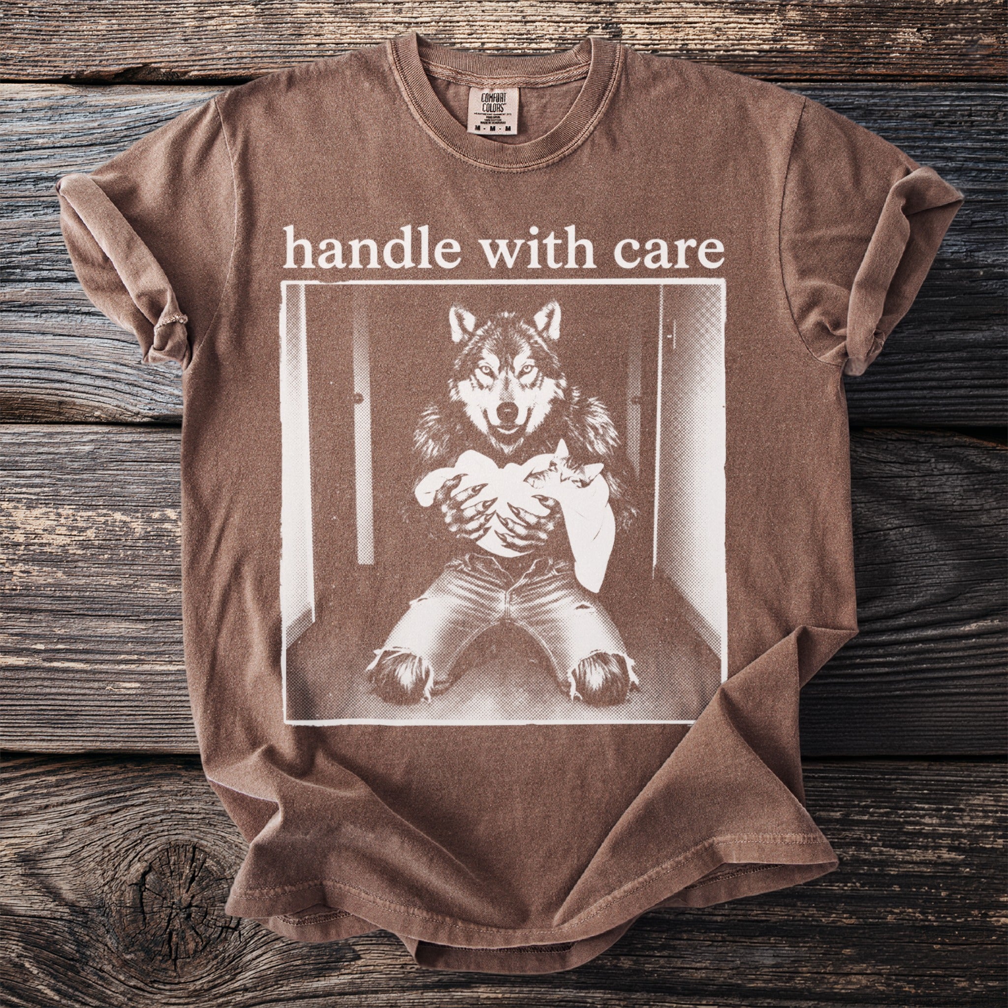 Brown t-shirt with graphic of wolf in jeans holding a baby and text "handle with care".