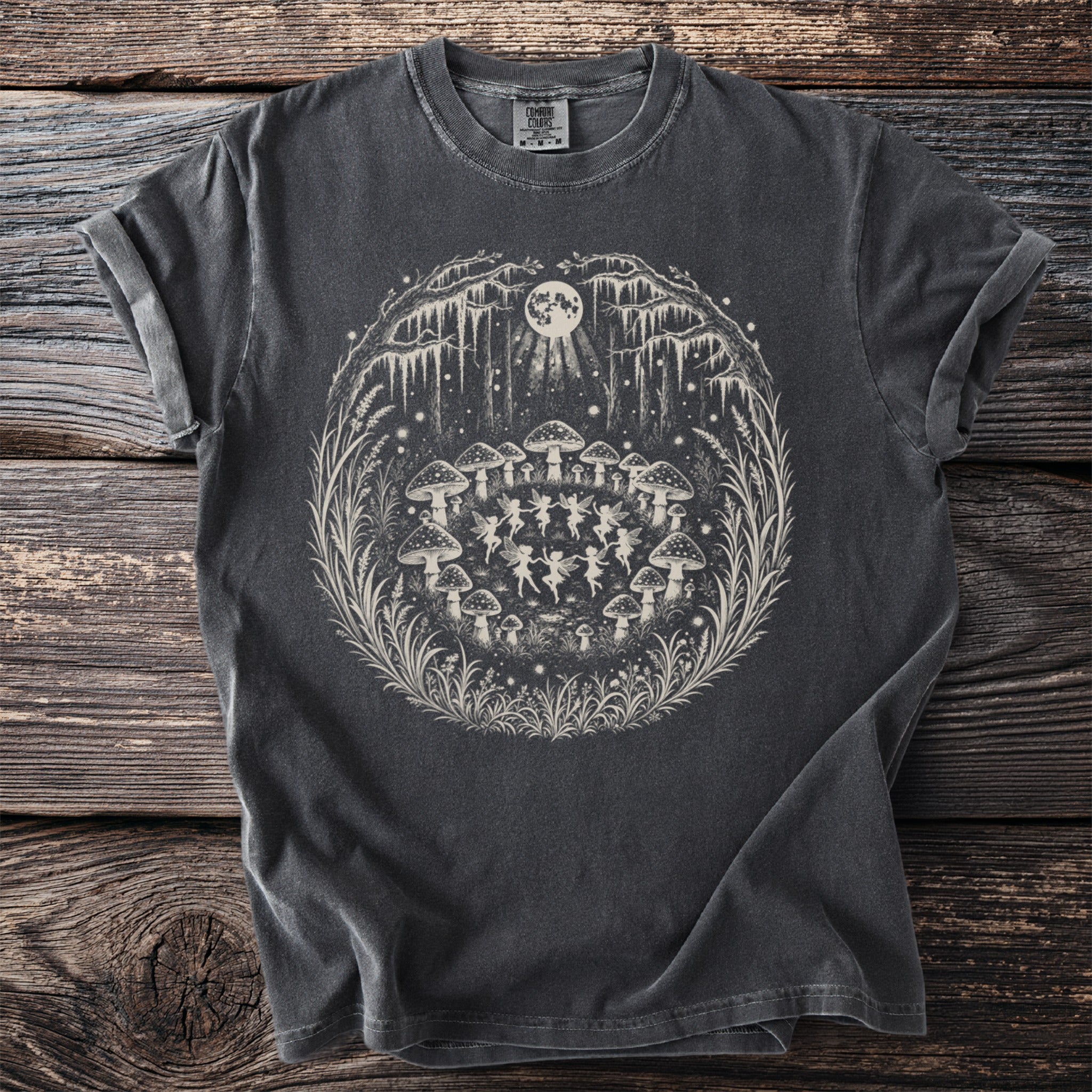 Dark grey t-shirt with white graphic of fairies dancing around mushrooms under a full moon.