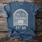 Blue t-shirt with an illustration of a witch's shelf filled with occult items.
