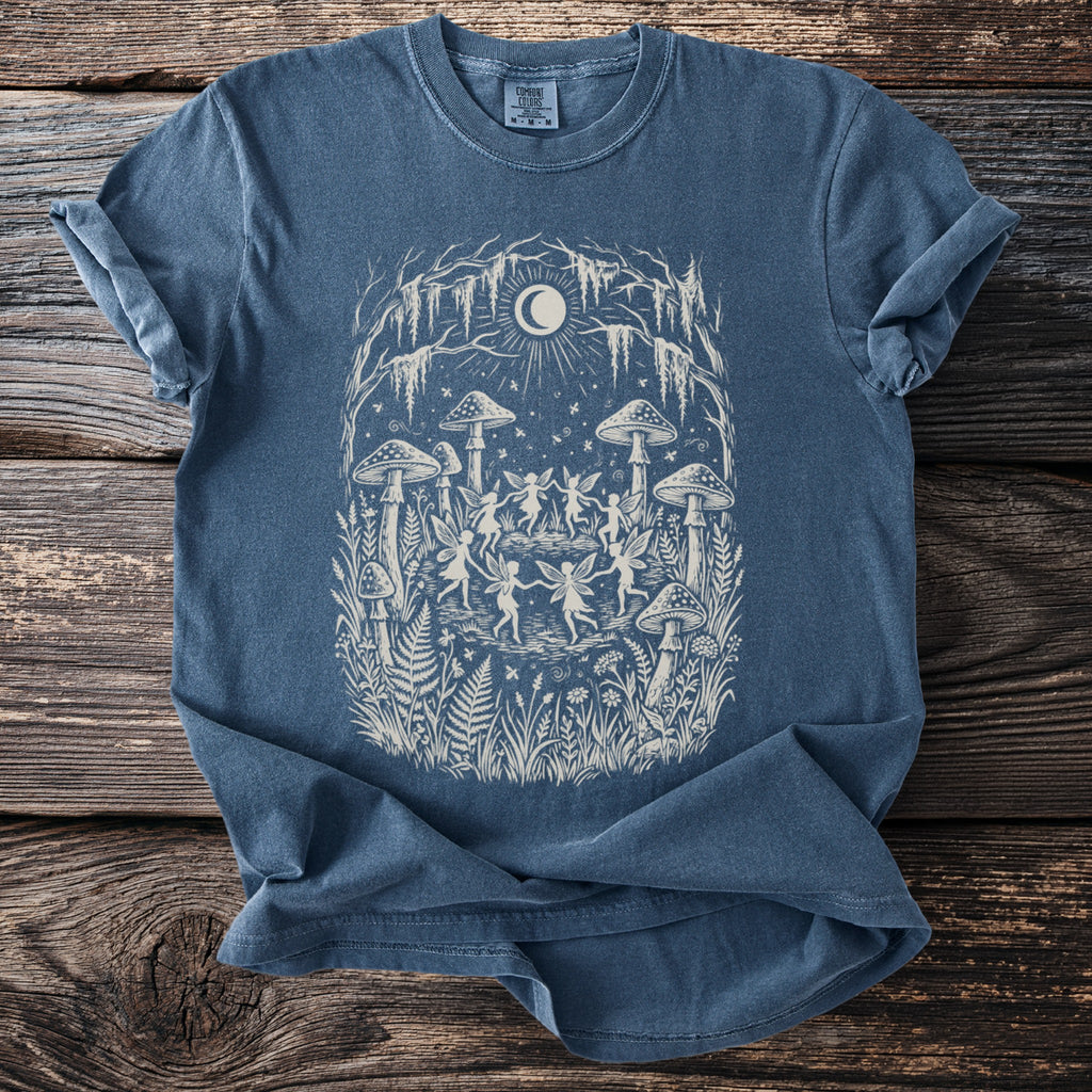 Blue t-shirt with a graphic of fairies dancing around mushrooms under a crescent moon.
