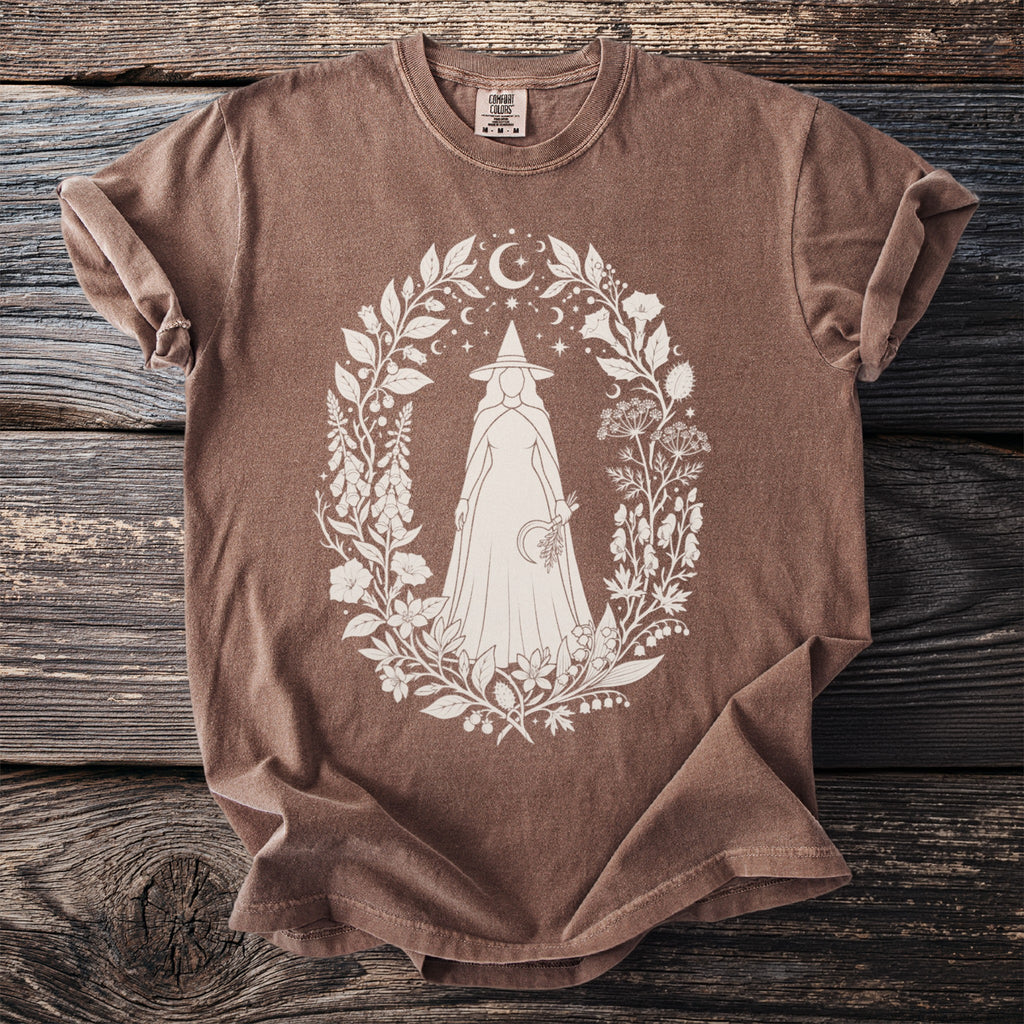 Brown t-shirt with white graphic of a cloaked figure within a floral and celestial wreath.