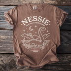 Brown t-shirt with white graphic of Nessie, castle, moon, and stars