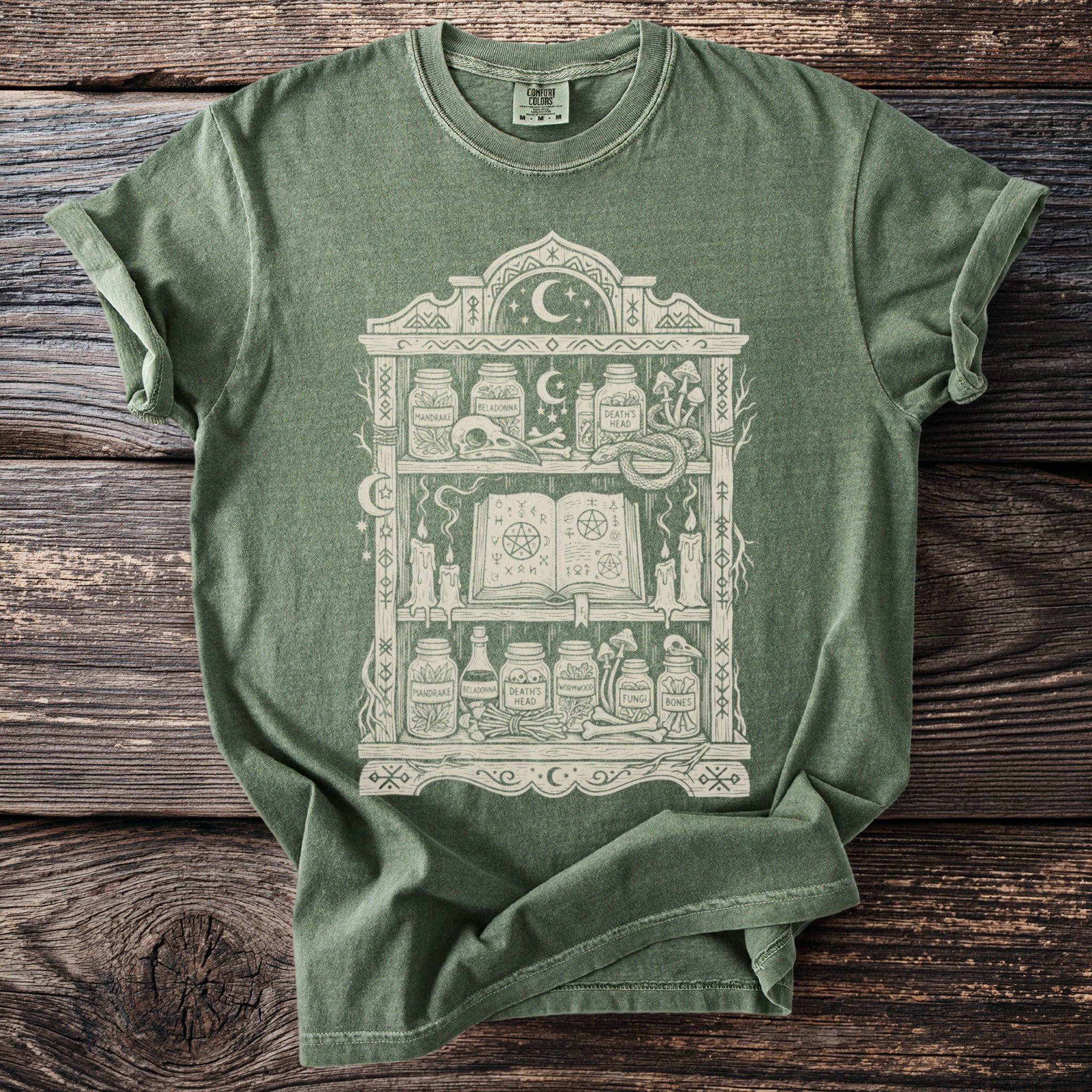 Green t-shirt with mystical apothecary shelf graphic and Comfort Colors tag.
