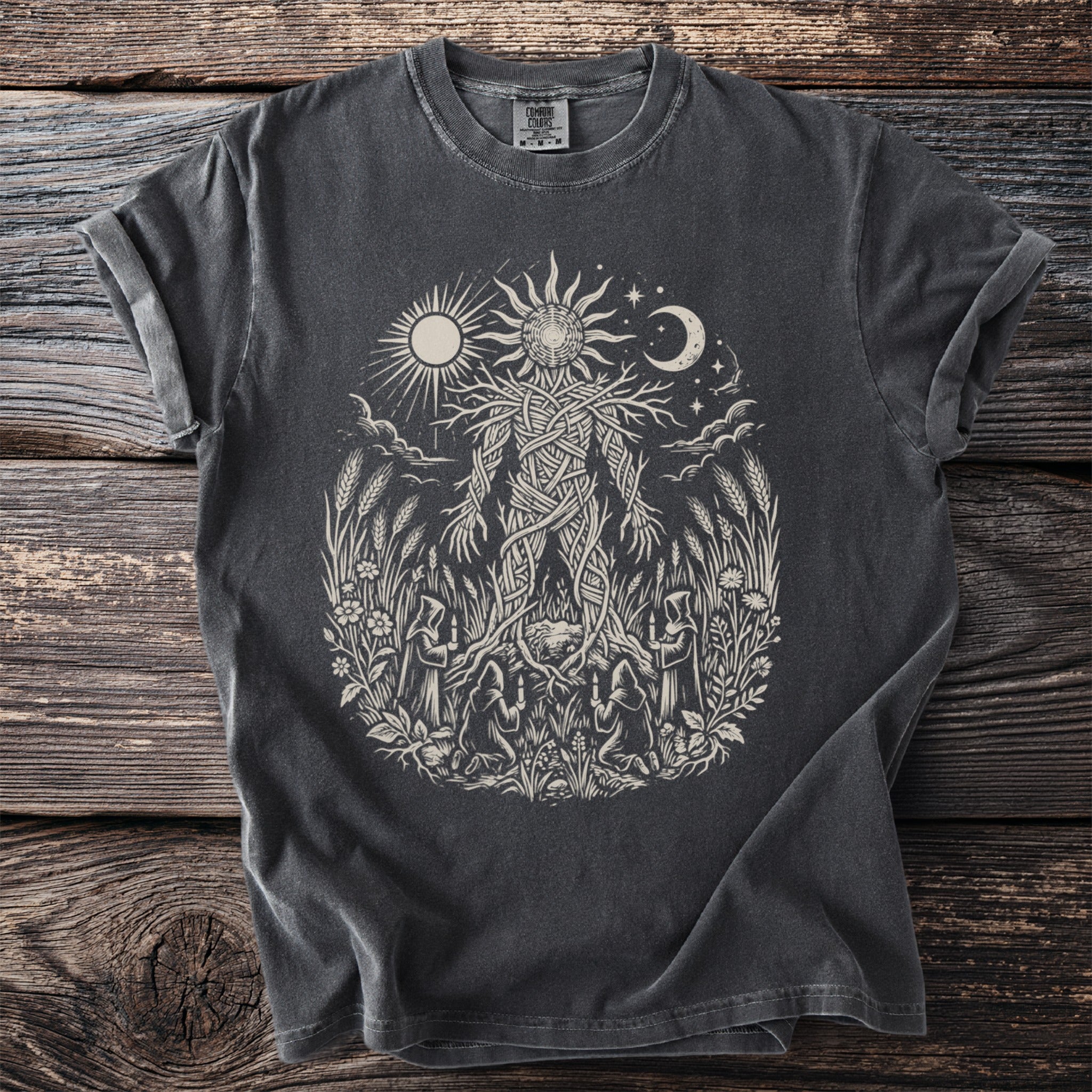 Dark grey t-shirt with a light-colored print of a woven figure surrounded by nature and figures.