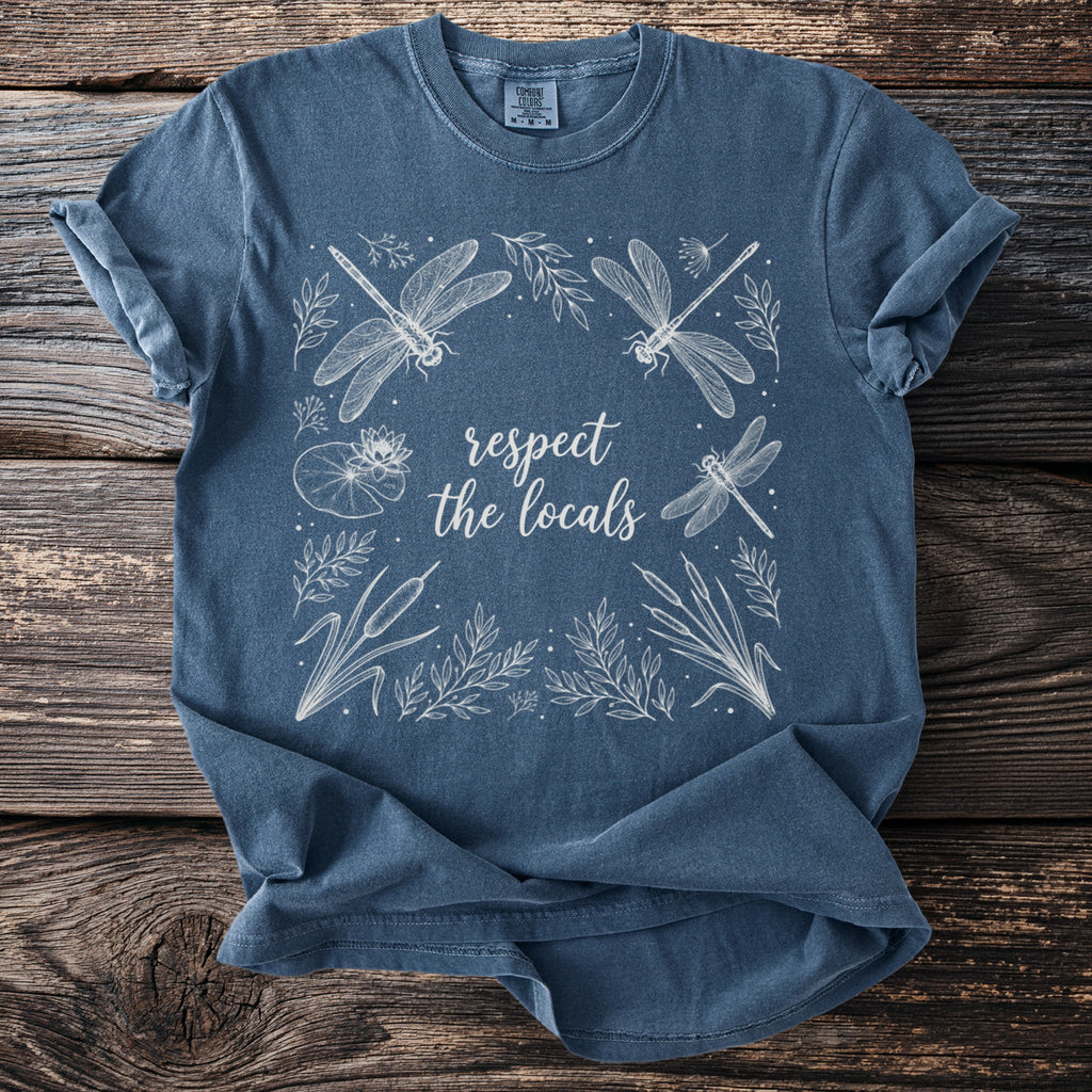 Blue t-shirt with white line art of dragonflies, lily pads, and cattails, featuring text "respect the locals".