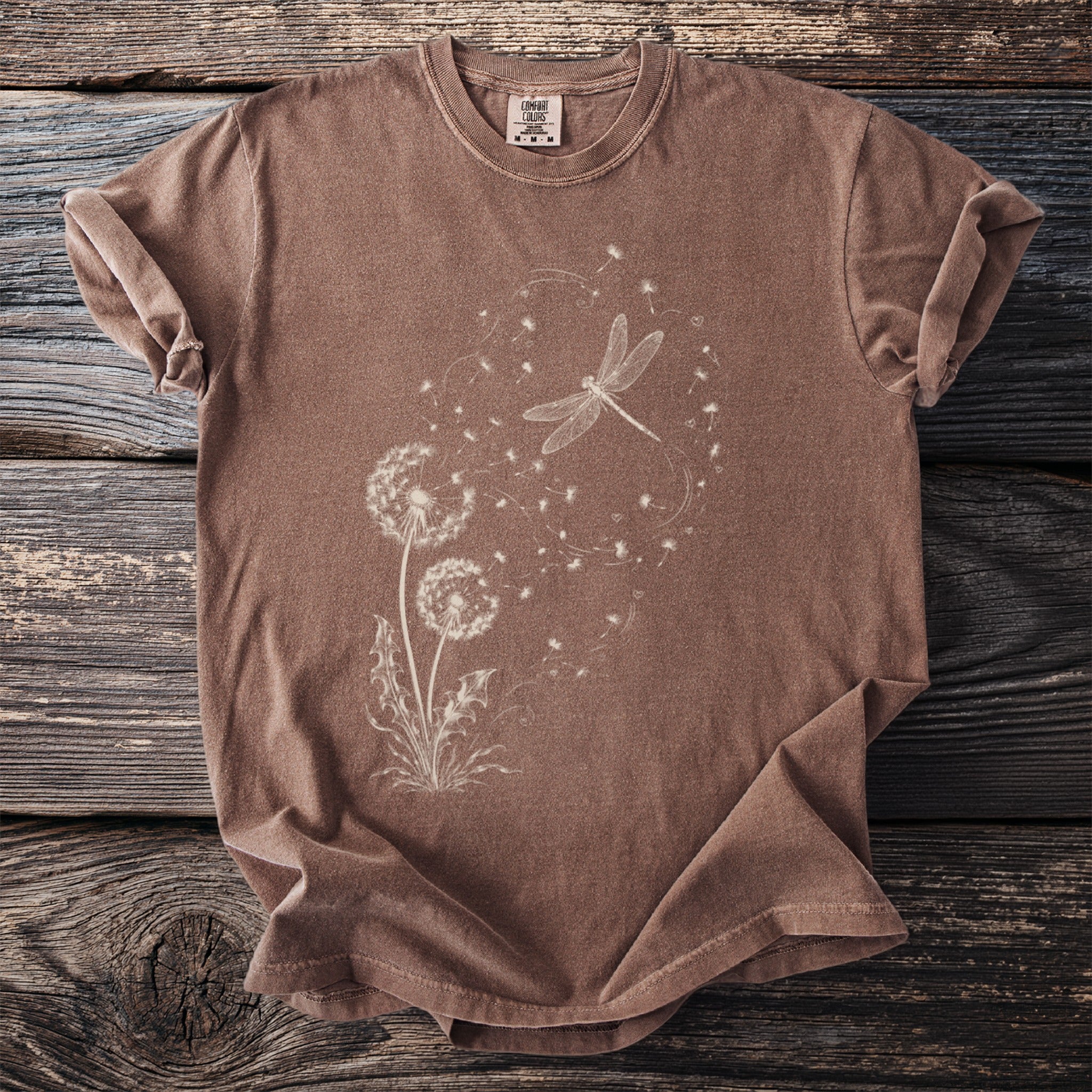 Brown t-shirt with a white dandelion and dragonfly graphic and Comfort Colors tag.