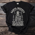 Black t-shirt with Santa Muerte folk outline graphic and text.