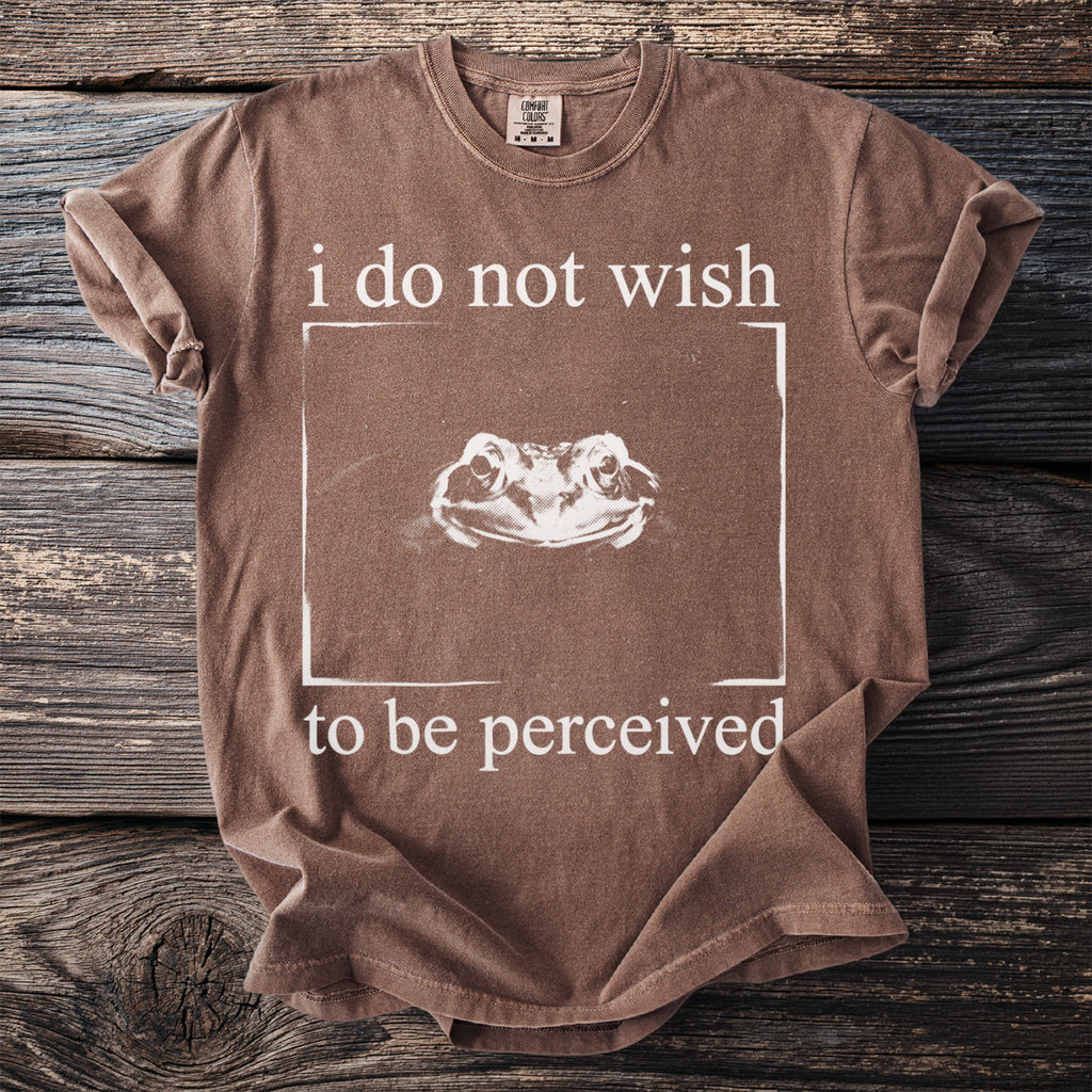 Brown t-shirt with white text "i do not wish to be perceived" and a frog illustration.