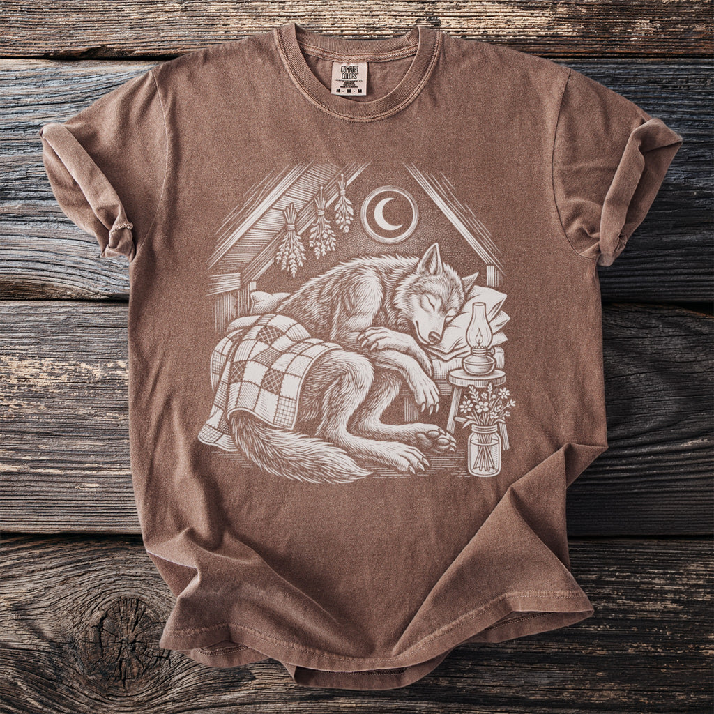 Brown t-shirt featuring a detailed illustration of a wolf sleeping peacefully under a checkered blanket.