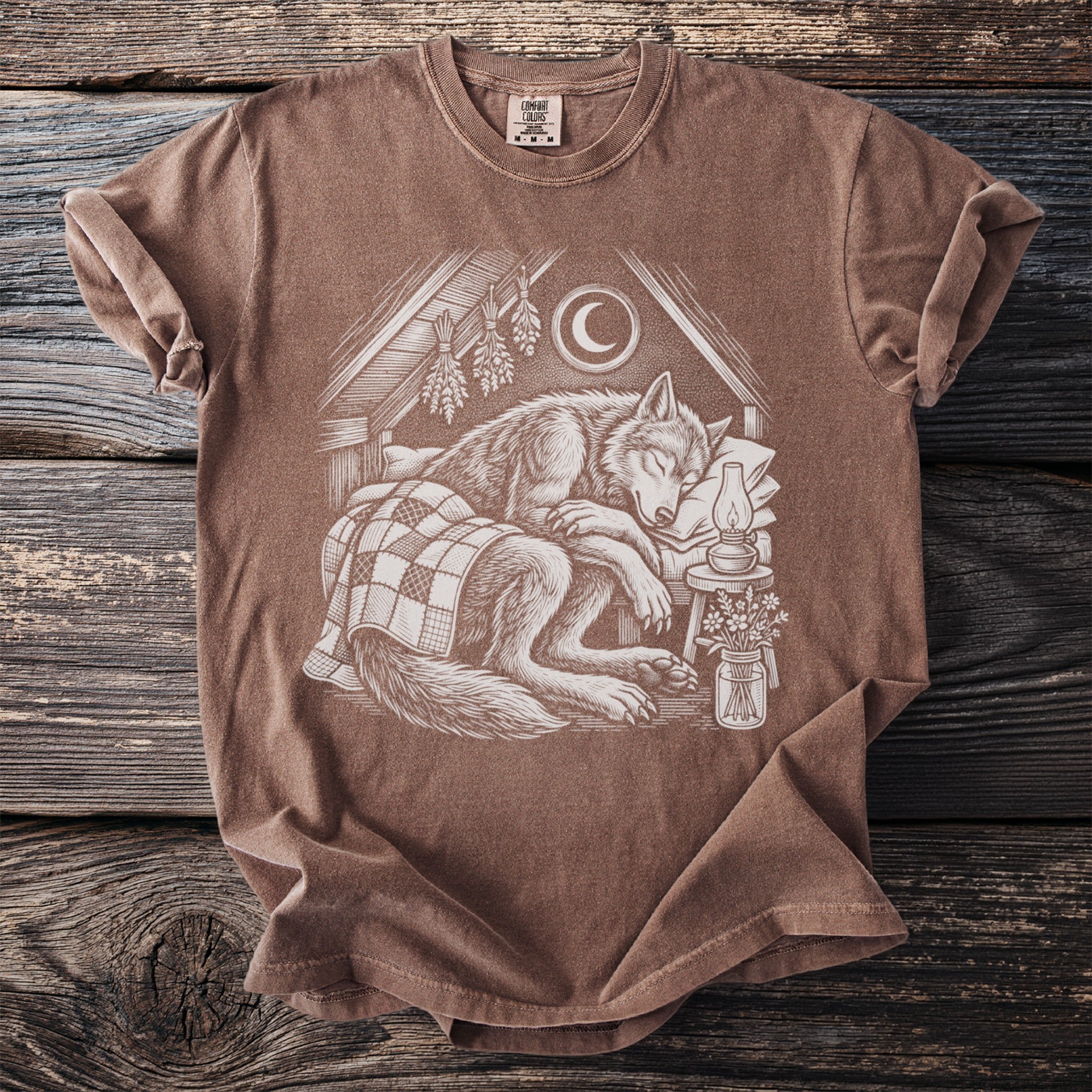 Brown t-shirt featuring a detailed illustration of a wolf sleeping peacefully under a checkered blanket.