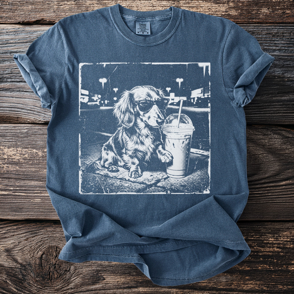 Dachshund wearing sunglasses next to a beverage on a t-shirt.