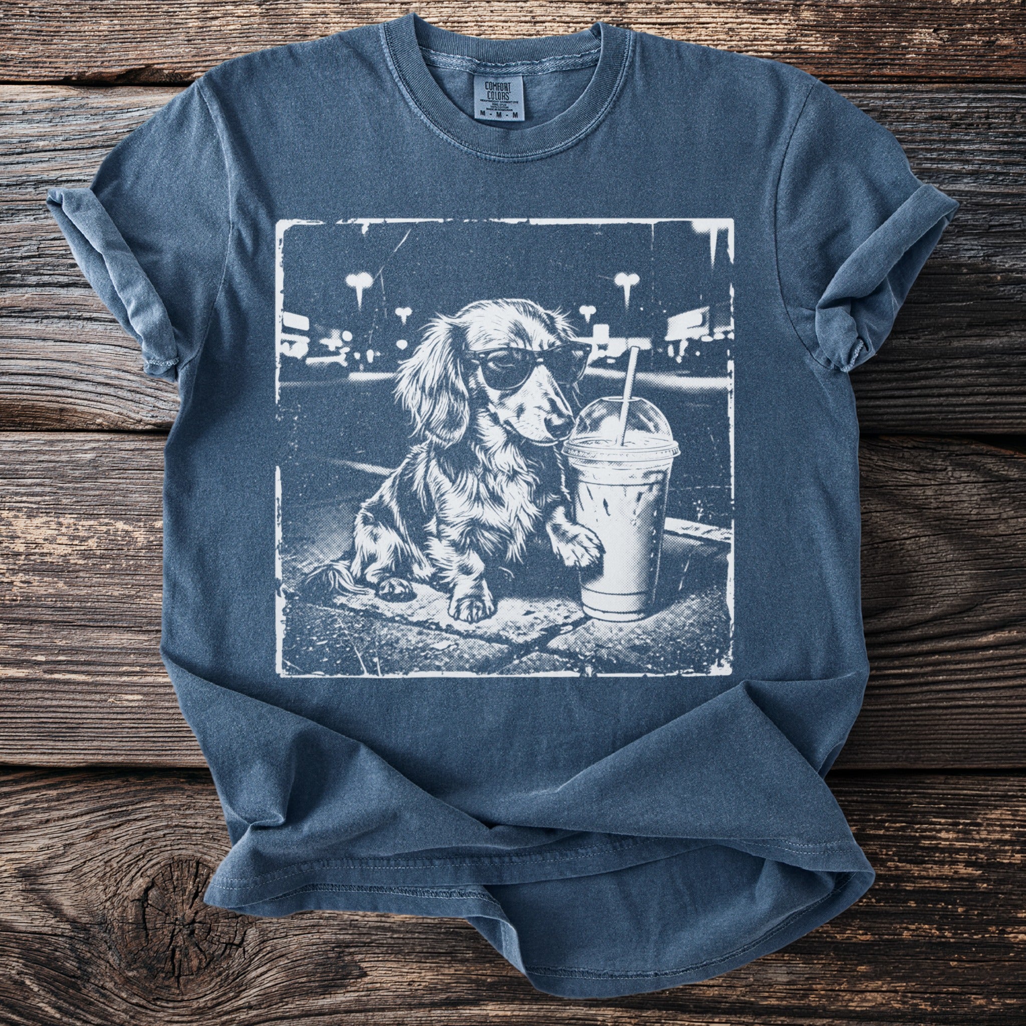 Dachshund wearing sunglasses next to a beverage on a t-shirt.