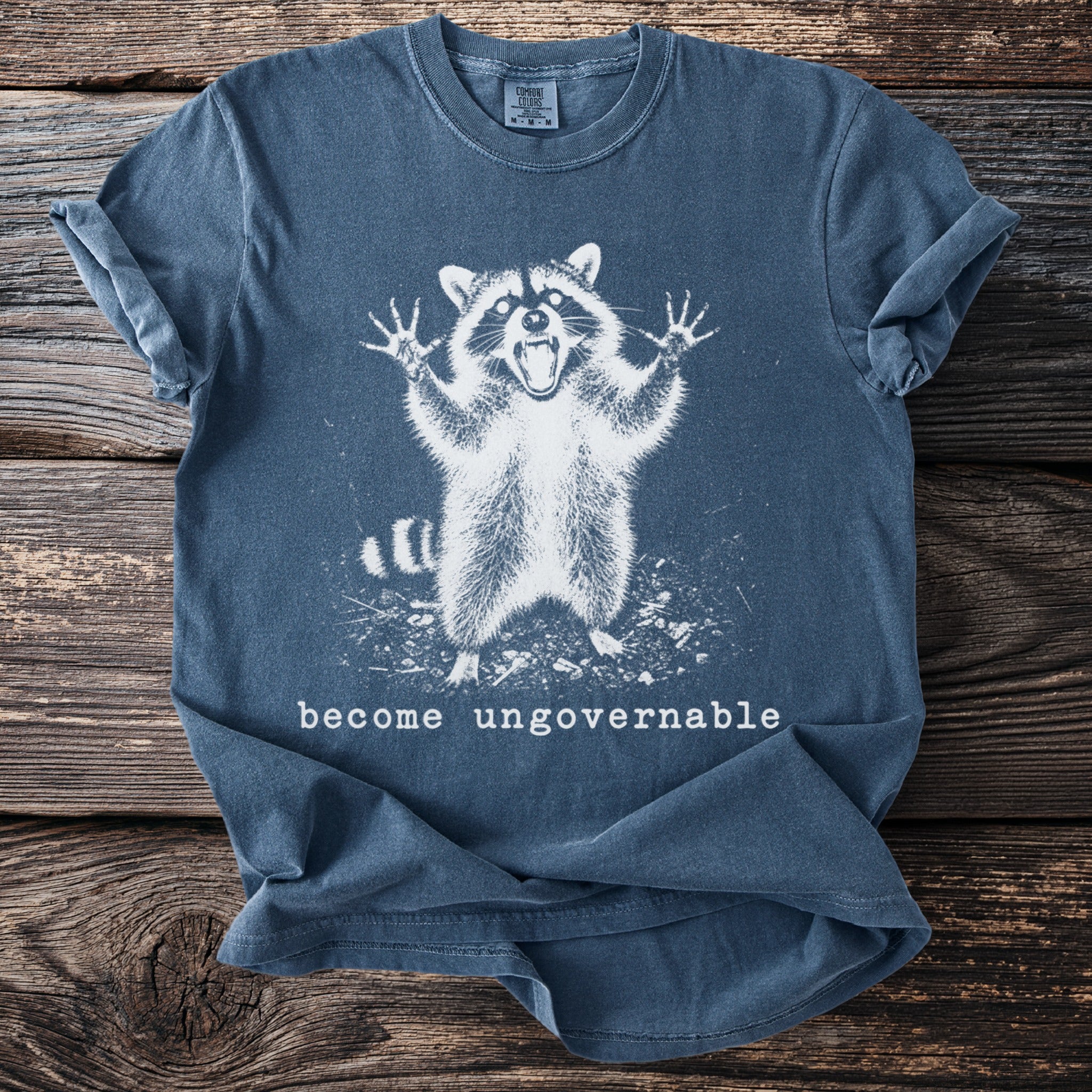 Blue t-shirt with screaming raccoon graphic and "become ungovernable" text.