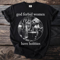 Black t-shirt with text "god forbid women have hobbies" and circular illustration.