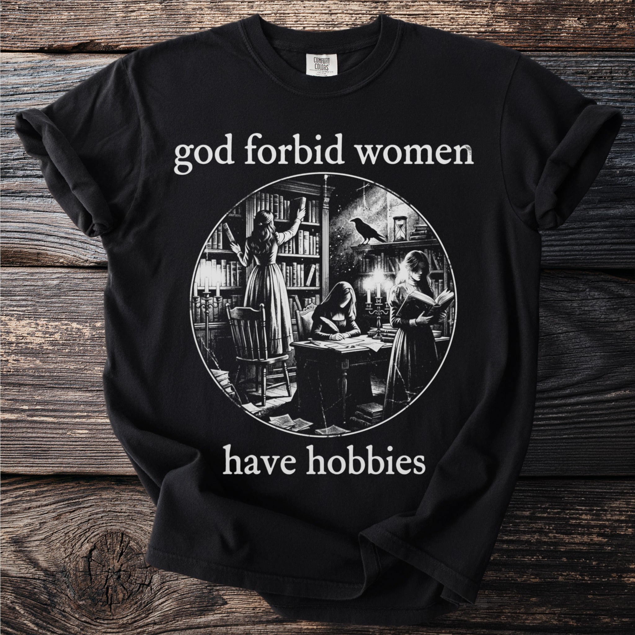Black t-shirt with text "god forbid women have hobbies" and circular illustration.