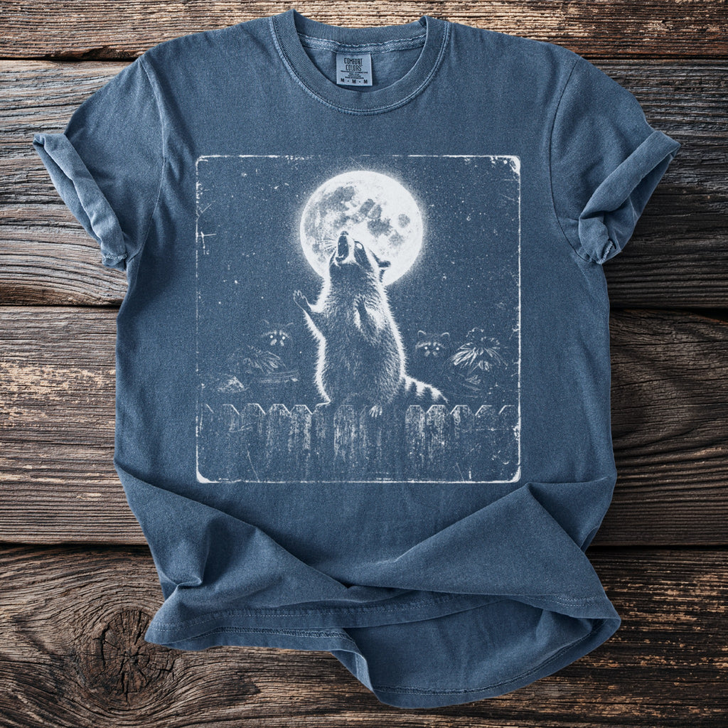 Blue t-shirt with a graphic of raccoons howling at the moon on a fence.